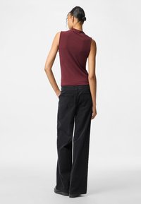 Top sin mangas burdeos con cuello alto; combinado con jeans negros de corte holgado y zapatos negros; textura suave y diseño simple.
