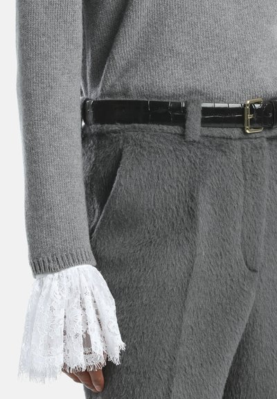 Pilkas megztinis su tekstūruotu paviršiumi, turintis baltus nėrinius su varpo formos rankogaliais. Suderinta su pilkomis kelnėmis ir blizgančiu juodu diržu su auksine sagtimi.