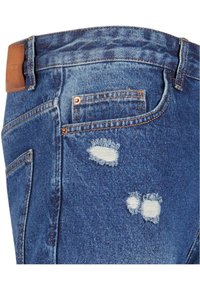 Jeans din denim cu un finisaj albastru deschis, prezentând detalii uzate cu margini desfăcute, o eticheta din piele pe talie și un design clasic cu cinci buzunare.