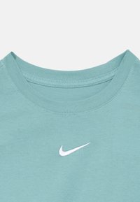 Svete teal bombažna majica z okroglo ovratnico in malim belim logotipom Nike natisnjenim na prsih. Gladka tekstura, sproščen kroj.