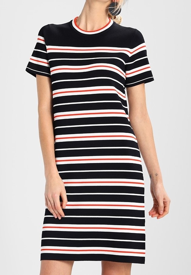 Femme portant une robe à manches courtes, longueur genou, avec des rayures horizontales noires, blanches et rouges sur un fond clair.