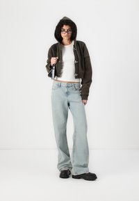 Cropped hooded jacket in dark olive with metal clasps, white fitted top, light wash wide-leg jeans, and black chunky shoes.