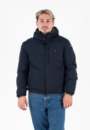 Marineblauwe pufferjack met capuchon, voorrits en borstzak. Gemaakt van een gladde, geïsoleerde stof met gele accenten op de manchetten.