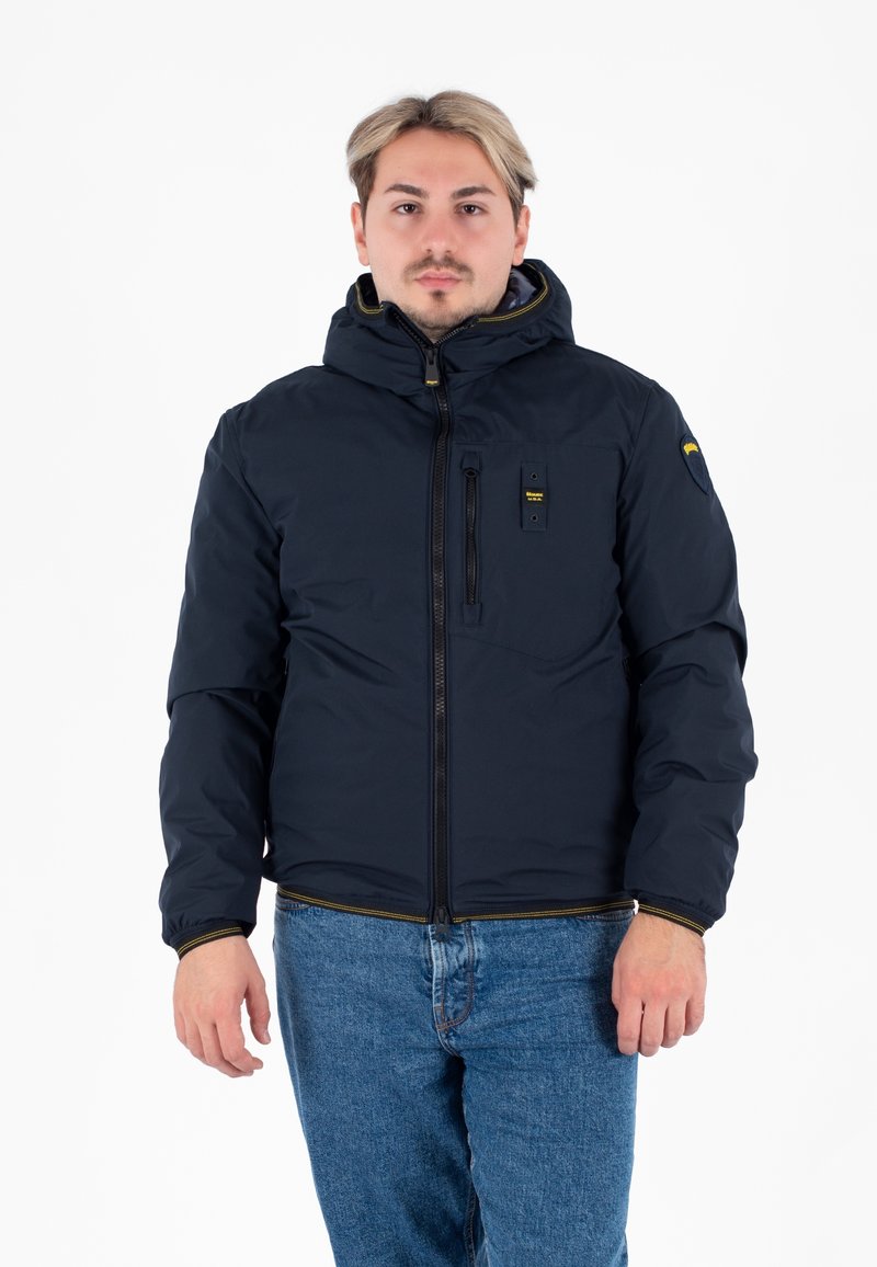 Granatowa kurtka puchowa z kapturem, zamkiem z przodu i kieszenią na piersi. Wykonana z gładkiego, izolowanego materiału z żółtymi akcentami na mankietach.