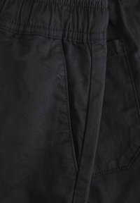 Pantalones cortos negros de tela suave, con una cintura elástica y bolsillos laterales. La costura es sutil y complementa el diseño general.