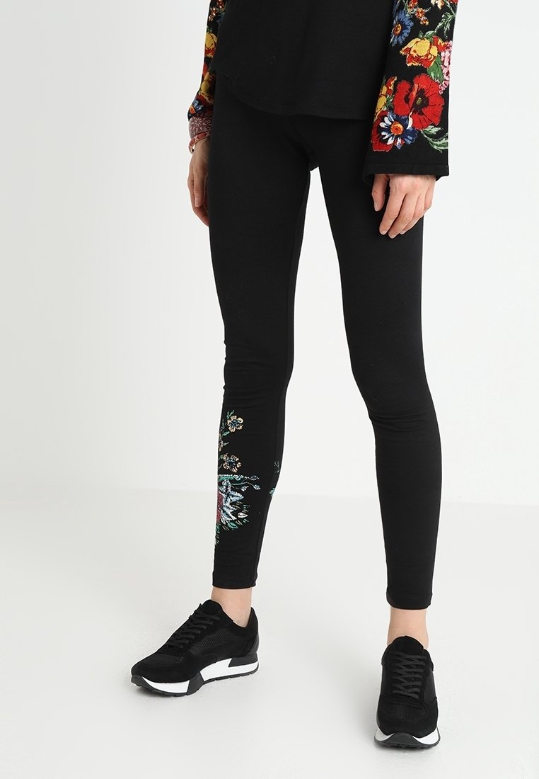 Černé legíny s květinovým vzorem na levé noze, s živými barvami. Doplnené černými sportovními botami. Měkký, elastický materiál.