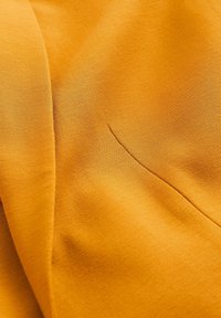 Gul tyg med en mjuk textur och subtil lyster, med en synlig sömmar detalj. Ytan är slät utan mönster eller accenter.