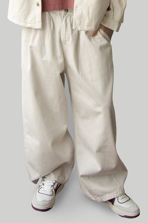 Light beige wide-leg cotton pants with an elastic waistband, featuring a relaxed fit and smooth texture, paired with white sneakers.