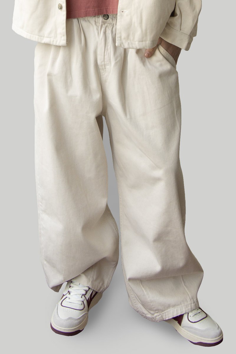 Pantalons larges en coton beige clair avec une taille élastique, présentant une coupe décontractée et une texture lisse, associés à des baskets blanches.