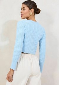 Světle modrý zkrácený svetr s strukturou kabelového pletení, slim fit dlouhé rukávy a žebrované manžety, doplněný o krémové skládací kalhoty.