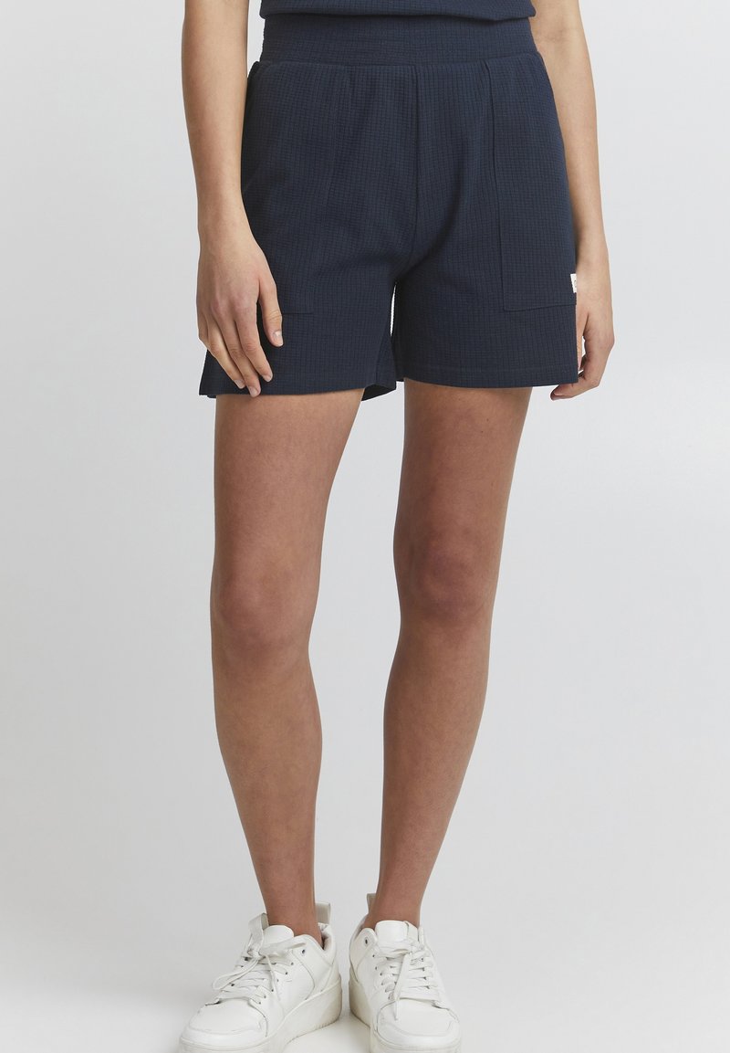 Marineblauwe shorts gemaakt van textuurstof, met een elastische tailleband, zijzakken en een rechte snit. Gemaakt in combinatie met witte sneakers.