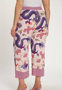 Roze stoffen broek met een draak- en bloemenpatroon. Voorzien van een rode geometrische tailleband en zoom, wijde pijpen en een gladde textuur.