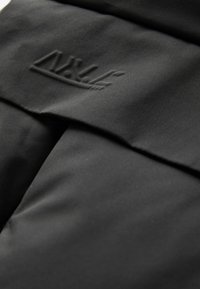 Pochette en tissu noir arborant un logo en relief discret. Le matériau présente une texture lisse et une finition mate, avec des détails de couture précis.