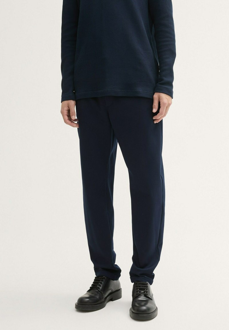 Granatowa prążkowana bluzka z długim rękawem w połączeniu z granatowymi spodniami, o luźnym kroju i jednolitym kolorze. Całość dopełniają czarne sznurowane buty.