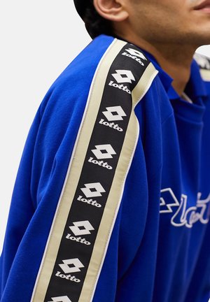 Blue sweatshirt with black and beige striped tape on sleeve featuring repeated white Lotto logos, worn by a person angled to the side.
