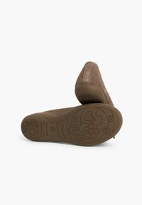 Zapatos tipo slip-on de ante marrón con punta redonda y suela de goma texturizada que presenta patrones de flores y corazones. La parte trasera es ligeramente elevada.