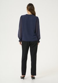 Marineblå bluse med tekstureret stof og gennemsigtige puffærmer. Matchet med sorte skræddersyede bukser og sorte hæle. Rynket detalje ved halsudskæringen.