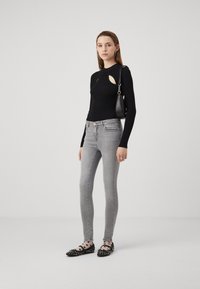 Svart ribbad långärmad topp med ett utskärningsdetalj, parat med ljusgrå tajta jeans och svarta lägenheter med vita prickar och nitar.