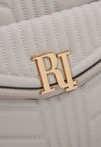 Sac en cuir matelassé gris clair avec des coutures verticales et un fermoir métallique doré avec le logo "RL" sur le rabat avant.