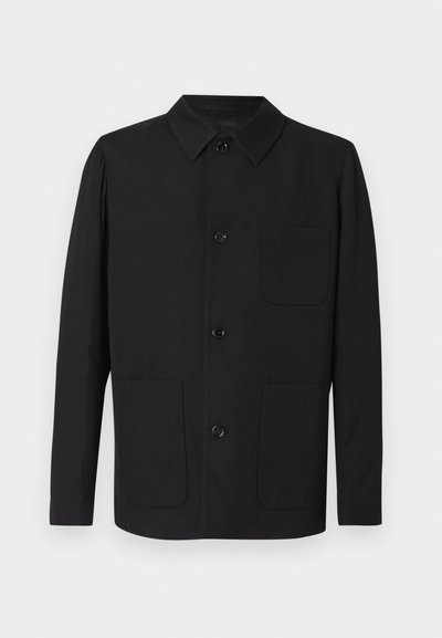 Μαύρο παλτό από λείο ύφασμα, με γιακά, κουμπιά μπροστά και δύο μεγάλες τσέπες. Απλός σχεδιασμός με ελάχιστες λεπτομέρειες.