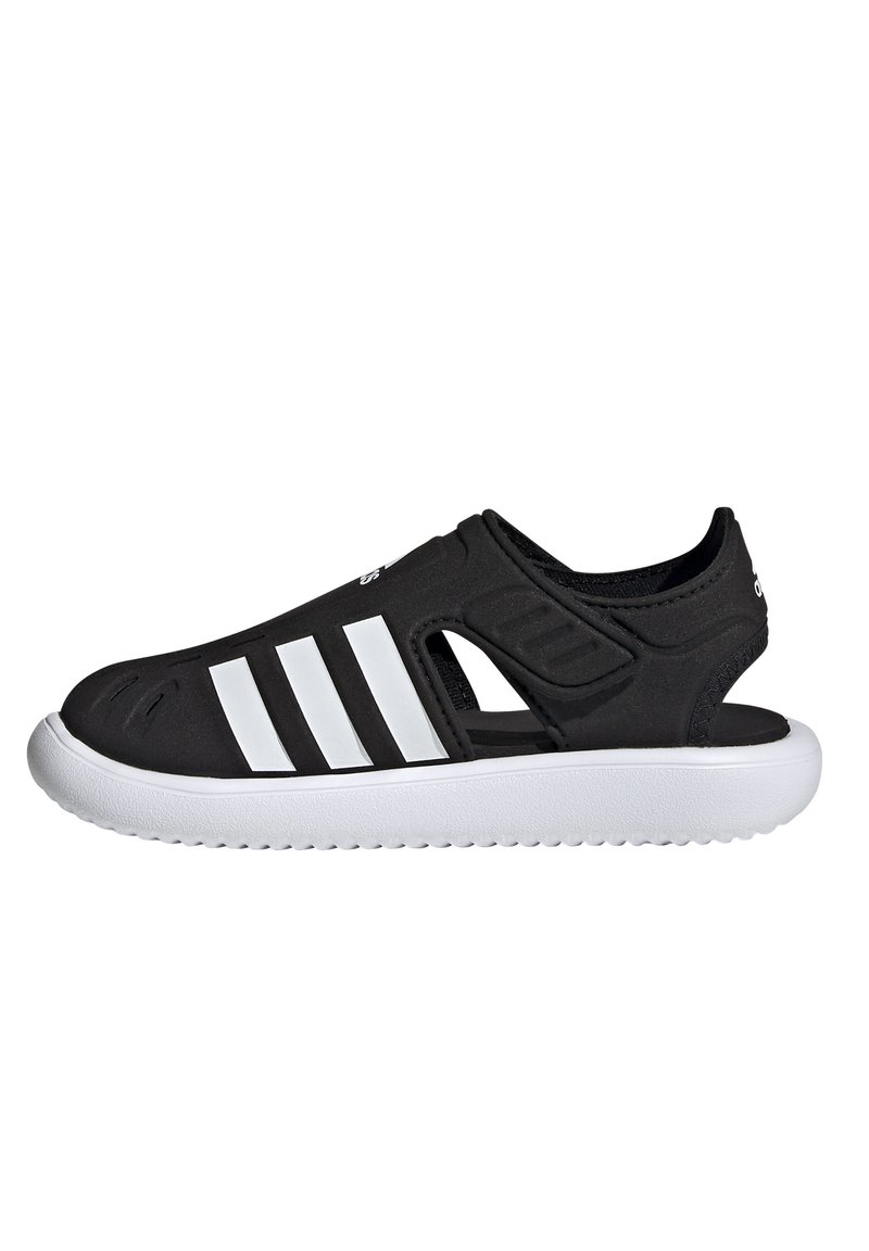 Sorte slip-on sko laget av syntetisk materiale, med utskårne seksjoner og tre hvite striper på siden, med en hvit gummisåle.
