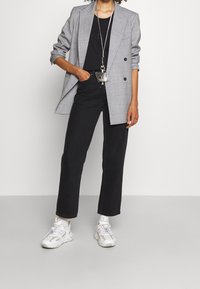 Blazer a cuadros grises con doble botonadura, combinado con una camisa negra y pantalones rectos negros. Zapatillas blancas completan el conjunto.