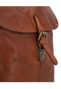 Gros plan sur le rabat d'un sac en cuir marron avec des bords cousus et une fermeture à boucle en métal fixant une sangle en cuir.