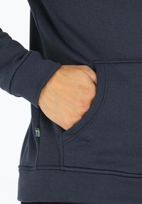 Felpa blu navy con una texture morbida, dotata di una tasca frontale e di un piccolo accento della bandiera svedese sul lato.