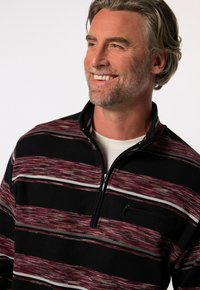 Czarny polar na zamek z poziomymi czerwonymi i białymi paskami. Zawiera małą kieszeń na zamek oraz ribbowaną strukturę. Dopasowany krój.