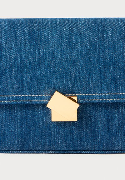 Porte-monnaie en denim avec un fermoir en forme de maison dorée ; texture douce avec des tons bleus et des coutures blanches contrastantes.