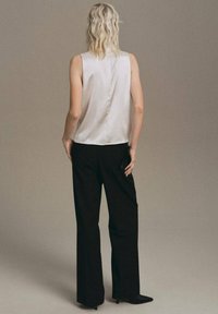 Satin, sleeveless top in off-white, featuring a subtle back seam; paired with high-waisted black trousers and pointed heels.