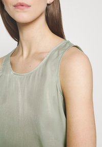 Top sin mangas de color verde claro, hecho de un tejido brillante, con un escote redondeado y costuras mínimas, que resalta una textura suave.