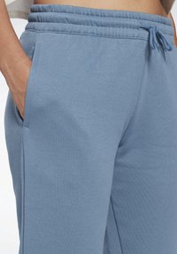 Blå bomullsjoggers med elastisk midja, sidofickor och en mjuk textur. Tyget har en jämn och slät yta.