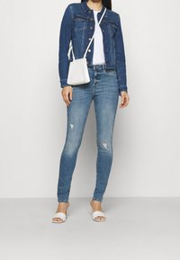 Mörkblå denimjacka med framfickor, matchad med ljusblå slitna skinny jeans, vit topp, vit handväska och vita sandaler.