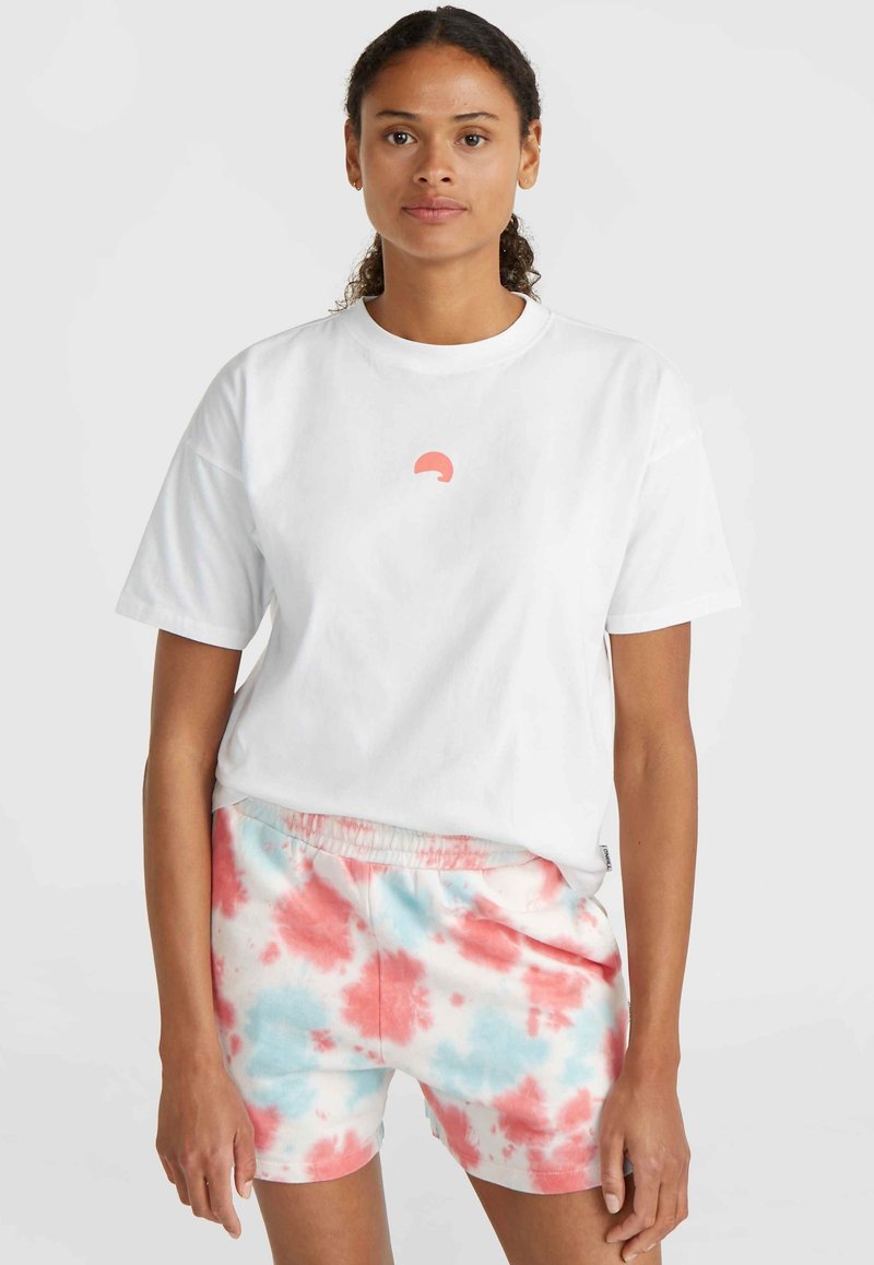 Weißes Baumwoll-T-Shirt mit einem kleinen rosa Halbkreis-Logo, kombiniert mit rosa und blauen Batikshorts mit elastischem Bund.