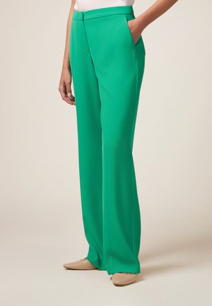 Groene wijde broek met een gladde textuur, uitgerust met zijzakken en een vlakke voorkant. Gepaarde met beige instapschoenen.