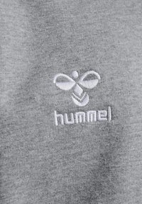 Grauer Baumwollstoff mit einem strukturierten, weißen gestickten Logo von "hummel" und einem stilisierten Design über dem Text.