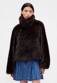 Maglione marrone in pelliccia con collo alto e maniche oversize, abbinato a una gonna di jeans con design a balze e cuciture visibili.