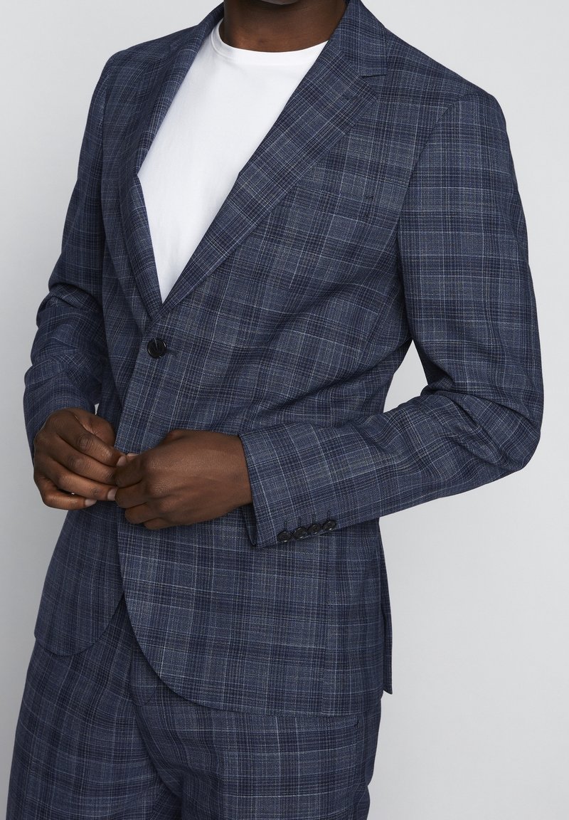 Marinblå rutig kavaj med notch laplar, en knappstängning och detaljer med fyraknappsmuddar. Bärs över en vit t-shirt.