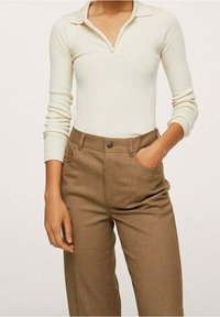 Kremowy, prążkowany top z długim rękawem z kołnierzykiem i zamkiem błyskawicznym do połowy, połączony z brązowymi spodniami o wysokim stanie z przednią kieszenią i zapięciem na guzik.