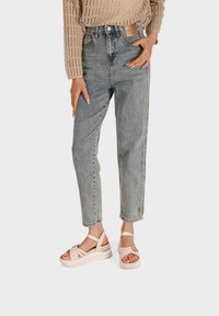 Jeans high-waisted di colore azzurro chiaro con una vestibilità rilassata e una texture sbiadita. Abbinate a sandali beige con cinturini e suola a piattaforma.