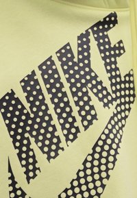 Felpa di un giallo chiaro con un grande logo grafico nero caratterizzato da un motivo a pois, che presenta in modo evidente la parola "NIKE". Texture liscia.