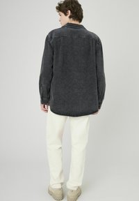 Chemise en denim gris foncé avec un motif floral, manches longues et ourlet arrondi. Associée à un pantalon blanc cassé et des chaussures beiges.