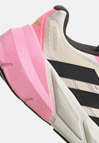 Chaussure de course avec un dessus rose et crème, accents noirs, matériaux synthétiques texturés et une semelle rembourrée proéminente.
