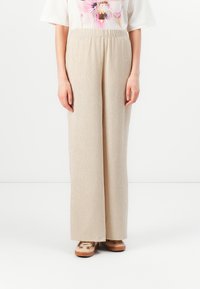 Beige, vida byxor med en texturerad yta och elastisk midja. Matchas med en lös, blommönstrad vit topp och lätta skor.