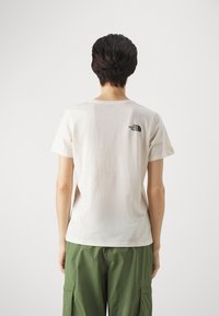 Camiseta de algodón color crema con mangas cortas, que presenta un pequeño logo negro en la parte superior de la espalda. Tejido texturizado, corte estándar.