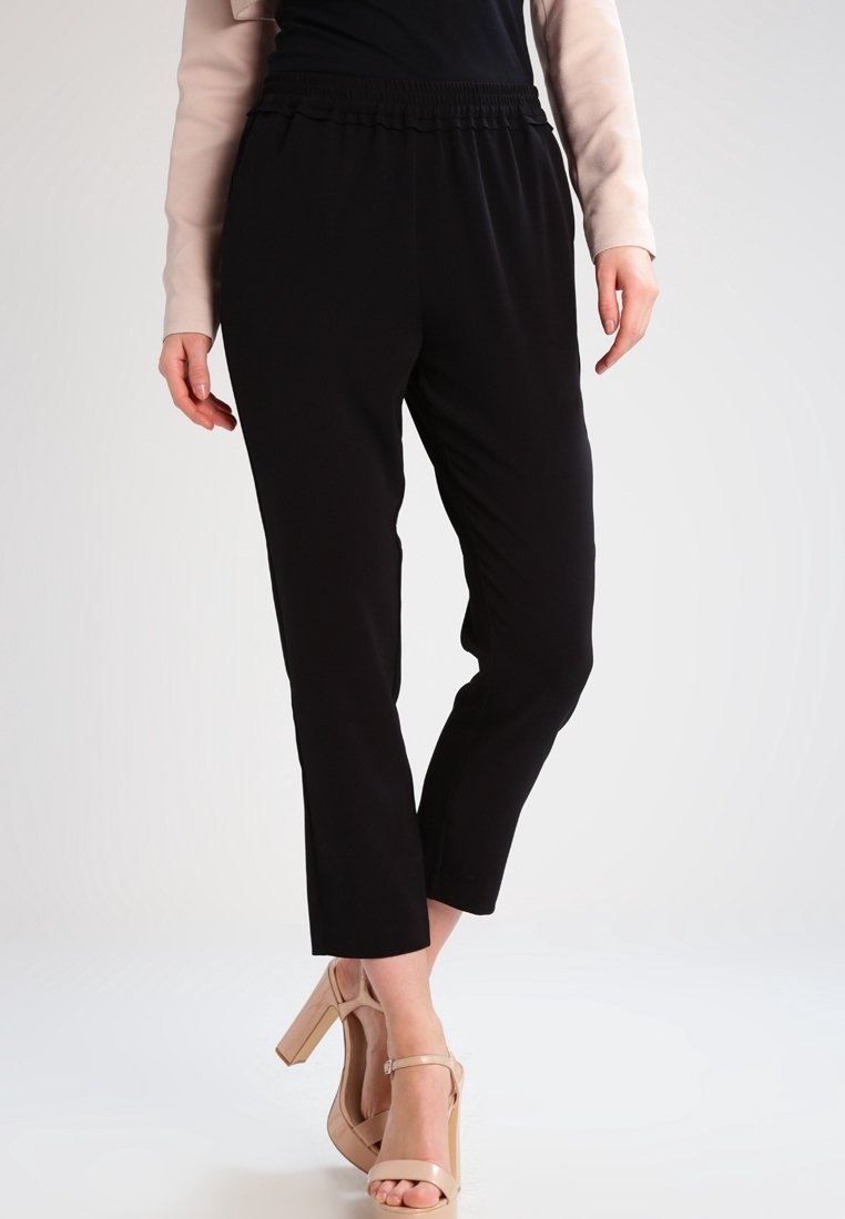 Black, tapered pants with an elastic waistband and a smooth, lightweight fabric. Paired with nude-strapped heels.