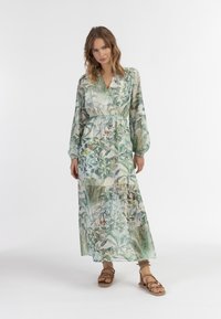 Rochie maxi florală dintr-un material ușor și transparent. Prezintă imprimeuri cu frunze verzi și albastre, cu mâneci lungi și o talie strânsă.