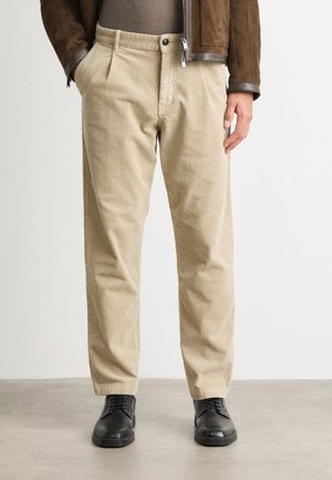 Beige corduroy trousers with a ribbed texture, featuring side pockets and a classic fit, paired with black lace-up shoes.
