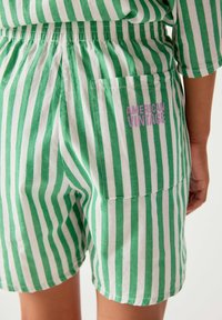 Gros plan d’un short rayé vertical vert et blanc avec une poche arrière étiquetée "American Vintage" en lettres roses.